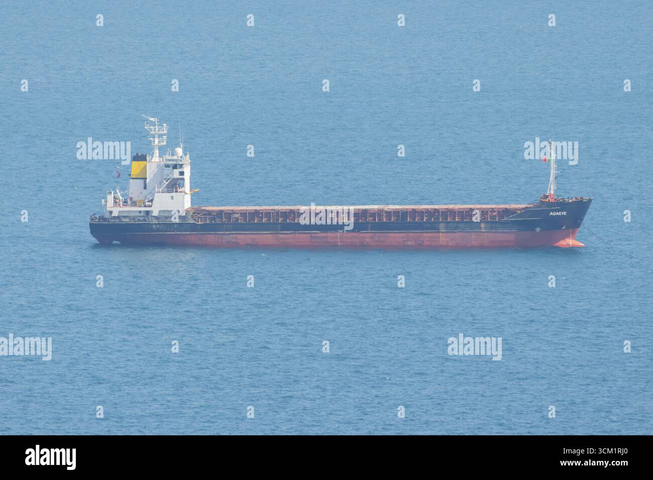 Großes Frachtschiff, das Güter über ein ruhiges Meer unter klarem blauen Himmel transportiert Stockfoto