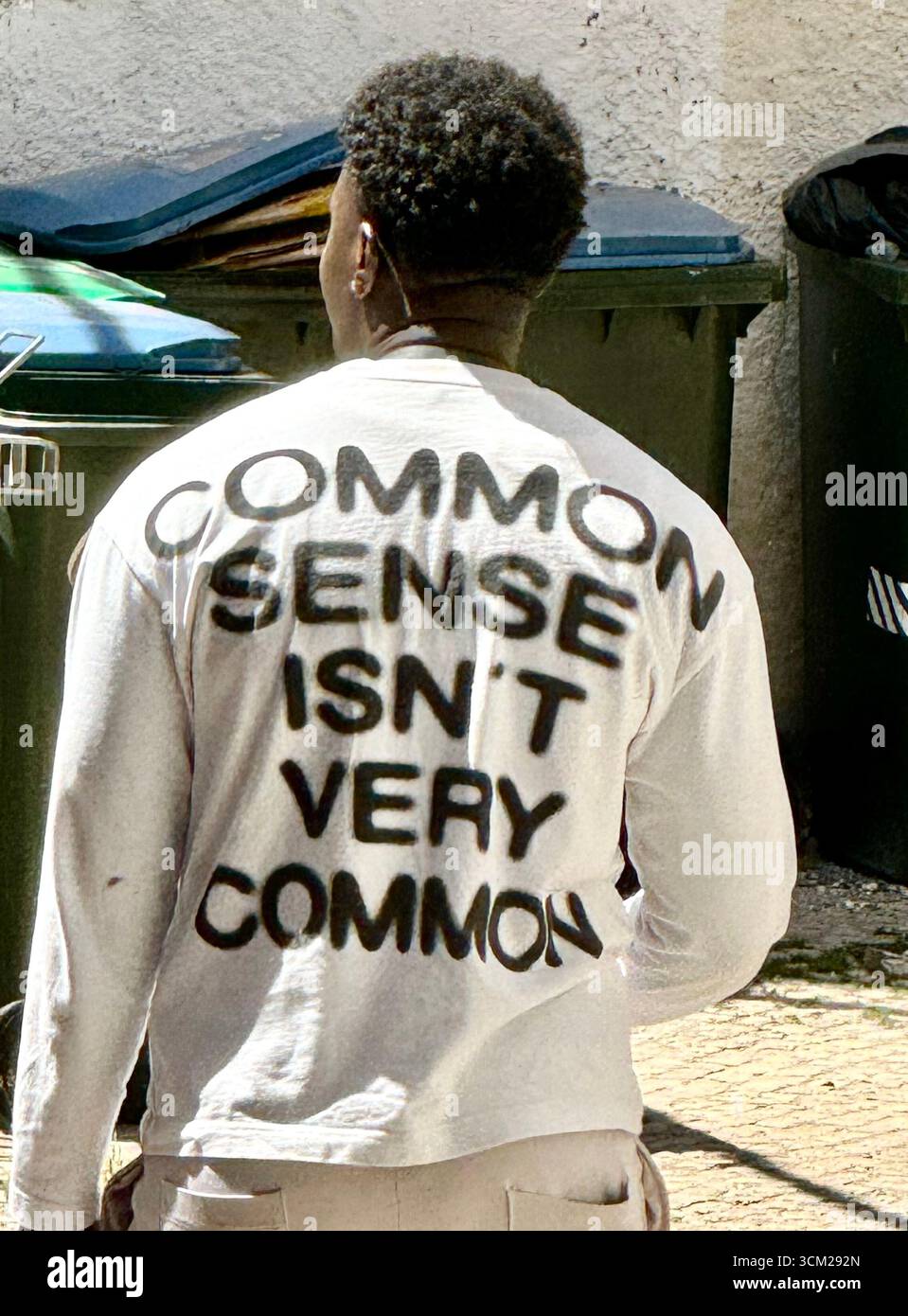 Afrikanischer Mann mit weißem Oberteil und humorvollem Slogan auf der Rückseite seines T-Shirts in Lissabon Portugal - Smartphone-aufgenommenes Stockfoto