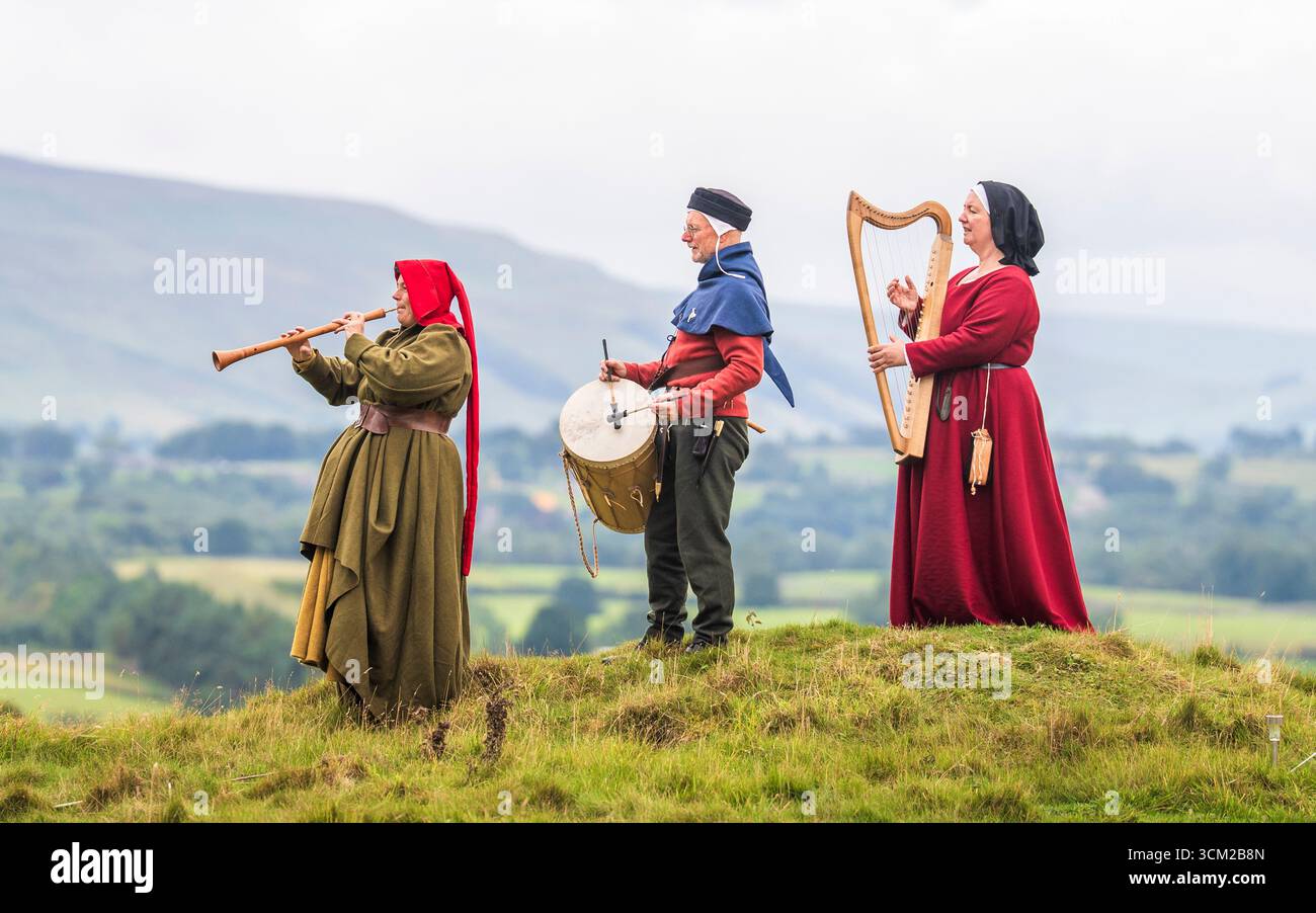 Von links nach rechts, Musiker in traditioneller Kleidung aus dem 15. Jahrhundert, Beck Laxton spielt einen Schal, Brad Chick spielt eine mittelalterliche Trommel und Jackie Phillips spielt eine bray Harfe während des Medieval Music in the Dales Festivals auf dem Gelände Bolton Castle in der Nähe von Leyburn, North Yorkshire. Das Festival findet in und um Bolton Castle statt, das 1399 von der adligen Familie Scrope erbaut wurde. Am Wochenende erwacht die Gegend mit Musik und lebendiger Geschichte zum Leben, da sie eine Gemeinschaft mittelalterlicher Musikbegeisterter zusammenbringt. Bilddatum: Sonntag, 14. September 2025. Stockfoto