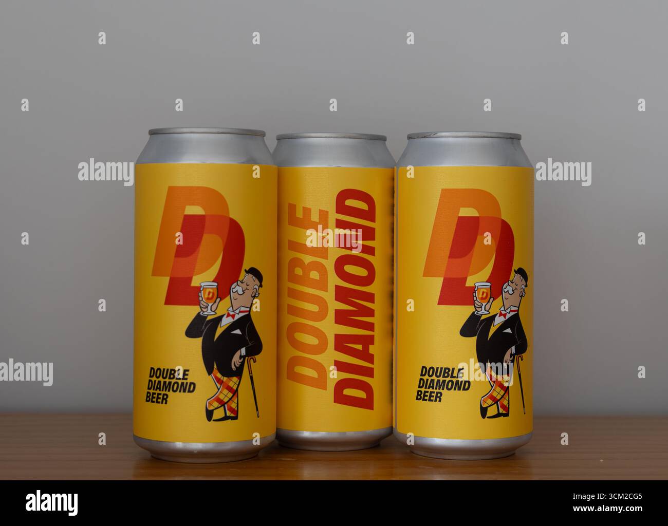 Drei Double Diamond Bierdosen mit leuchtend gelber Verpackung und einer Vintage-Illustration auf einer Holzoberfläche Stockfoto