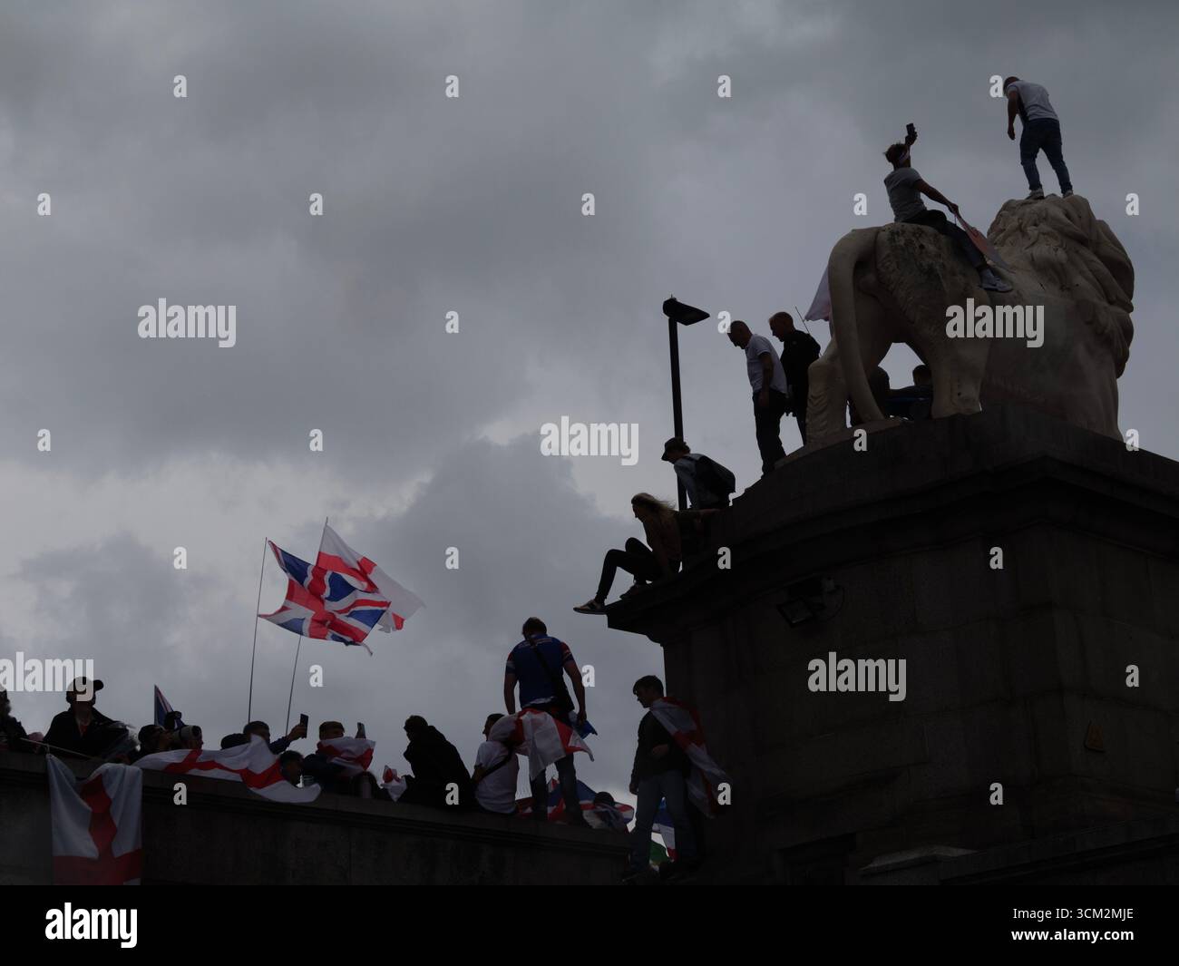 Unite the Kingdom Protest, 13. September 2025, Westminster, London, Großbritannien. Unter dunklen Wolken kletterten Demonstranten mit den Flaggen von Union Jack und St. George auf dem South Bank Lion auf der Westminster Bridge in Central London auf einem Protest, der von Tommy Robinson organisiert wurde Stockfoto