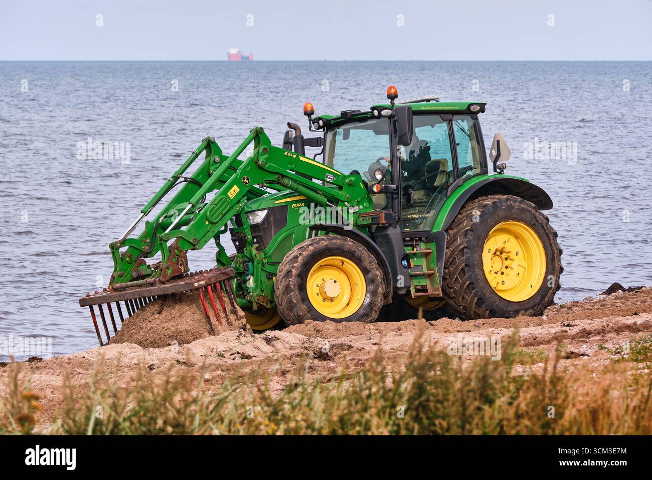Helsingborg, Schweden; 12. August 2025: John Deere Traktor kratzt Algen aus Sand mit Rechen während der detaillierten Strandreinigung. Stockfoto