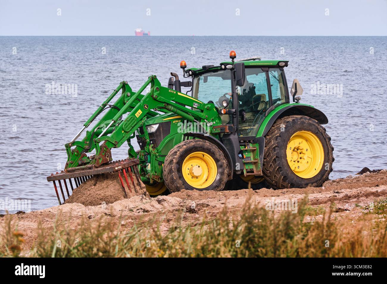 Helsingborg, Schweden; 12. August 2025: John Deere Traktor kratzt Algen aus Sand mit Rechen während der detaillierten Strandreinigung. Stockfoto