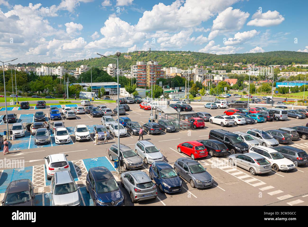 Geräumiger Außenparkplatz mit vielen Autos, umgeben von landschaftlich reizvollem Grün in der Einkaufsstadt Târgu Mureș, Rumänien Stockfoto