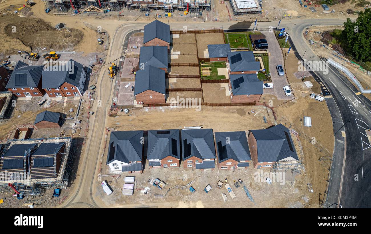 Aus der Vogelperspektive eines im Bau befindlichen Vorstadtgebäudes mit Ziegelhäusern mit dunkelgrauen Dächern, einige mit Solarpaneelen und verschiedenen Konsolen Stockfoto