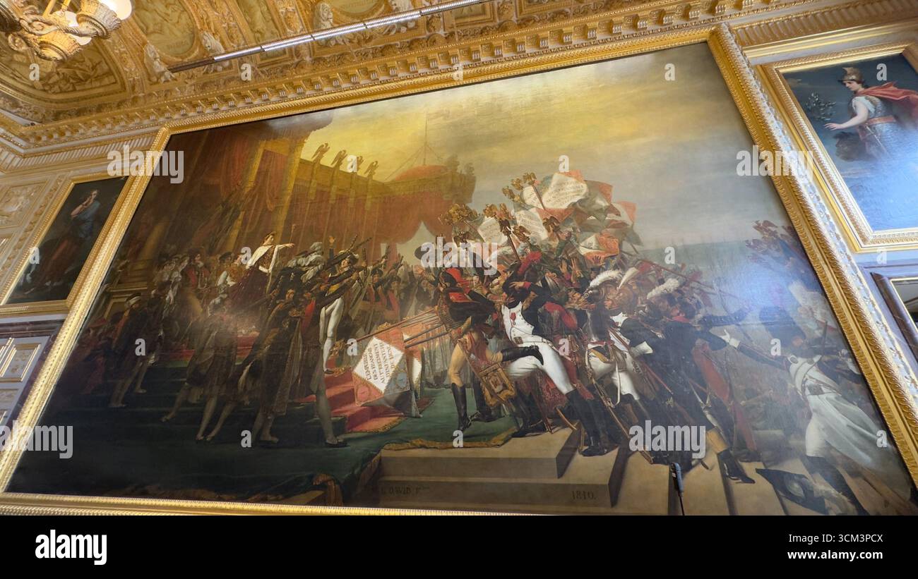 In einem großen, vergoldeten Saal sind große Ölgemälde ausgestellt. Das zentrale Kunstwerk zeigt eine historische Szene mit zahlreichen Figuren und Fahnen unter hellem Himmel, ri Stockfoto