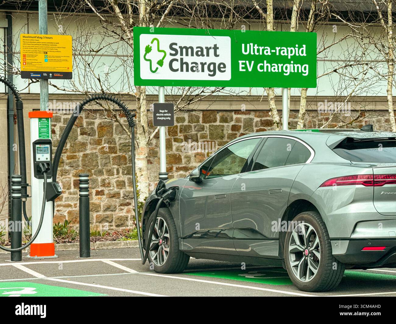 Bridgend, Wales, Vereinigtes Königreich - 26. März 2025: Auto in einer Parkbucht an ein Terminal zum Aufladen von Elektrofahrzeugen in einem Supermarkt angeschlossen. Keine Personen. - Smartphone-aufgenommenes Stockfoto