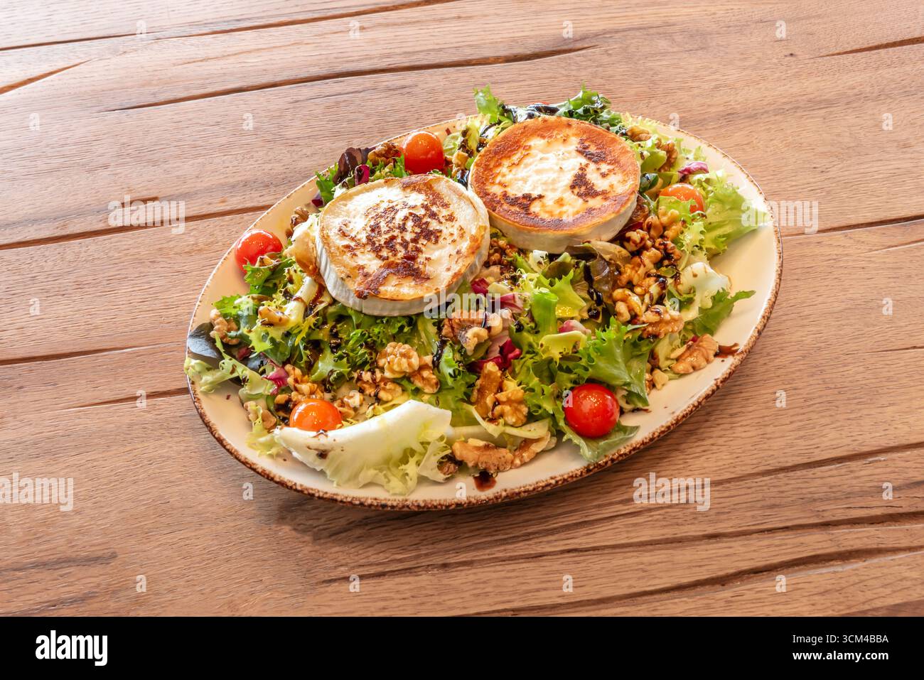Warmer, geschmolzener Ziegenkäsesalat auf einem Eichenblatt-Salatbett, geröstete Kirschtomaten und knusprige Roggenbrotcroutons Stockfoto