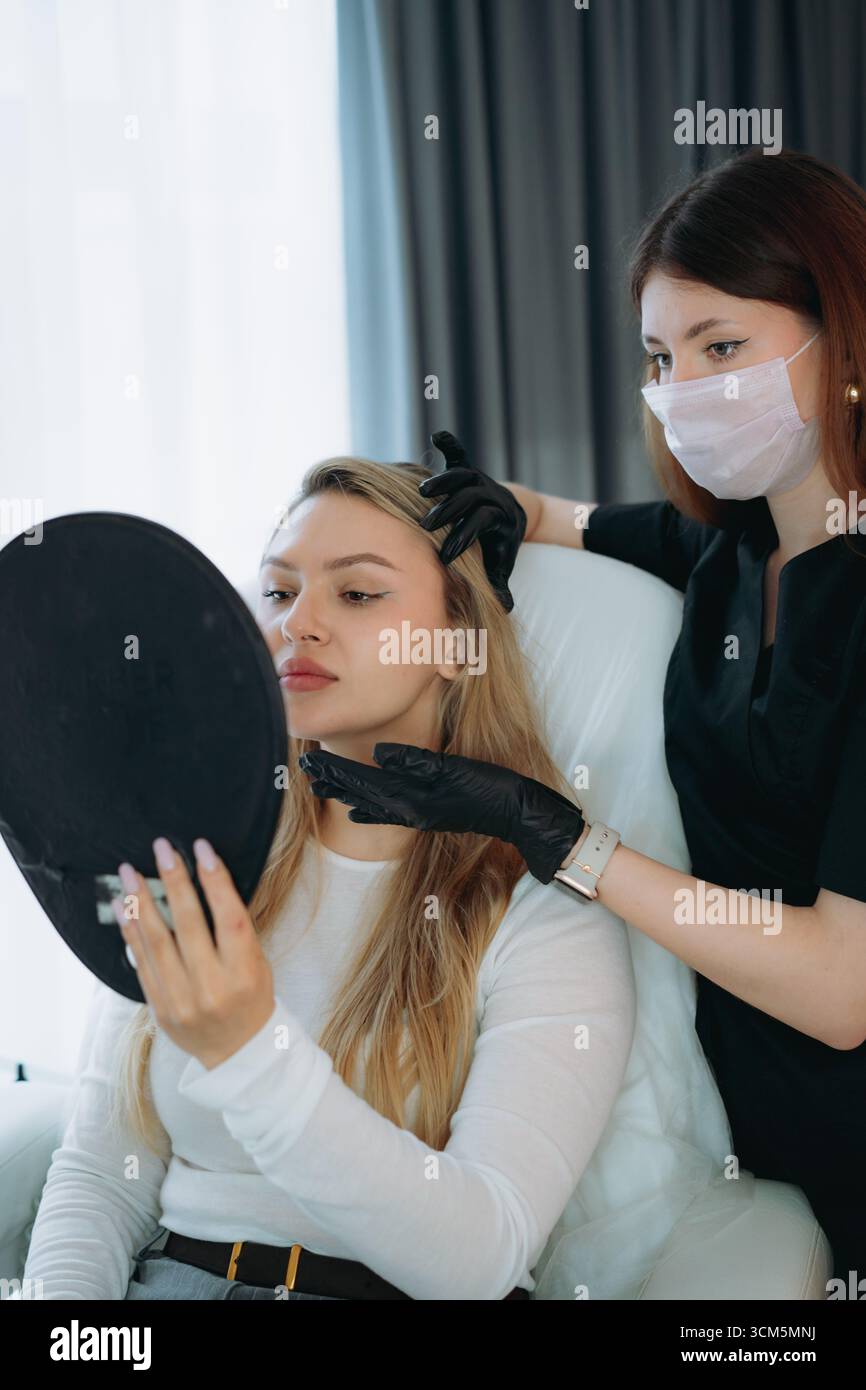 Ästhetische Ärztin bei personalisierter Anti-Aging-Beratung mit einer jungen Kundin mit Spiegel Stockfoto