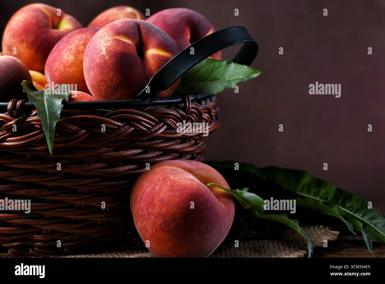 Stillleben eines braunen gewebten Korbs, gefüllt mit gelben Pfirsichen mit fleckigem Hintergrund und Kopierraum. Stockfoto
