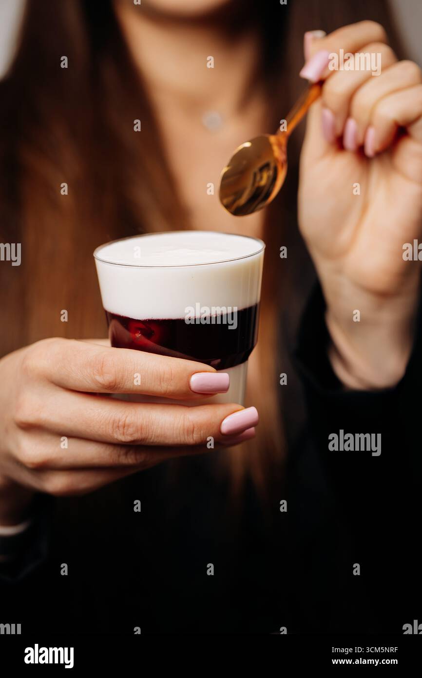 Frau mit cremigem Dessert mit Kirschgelee im Glas und goldenem Löffel Stockfoto