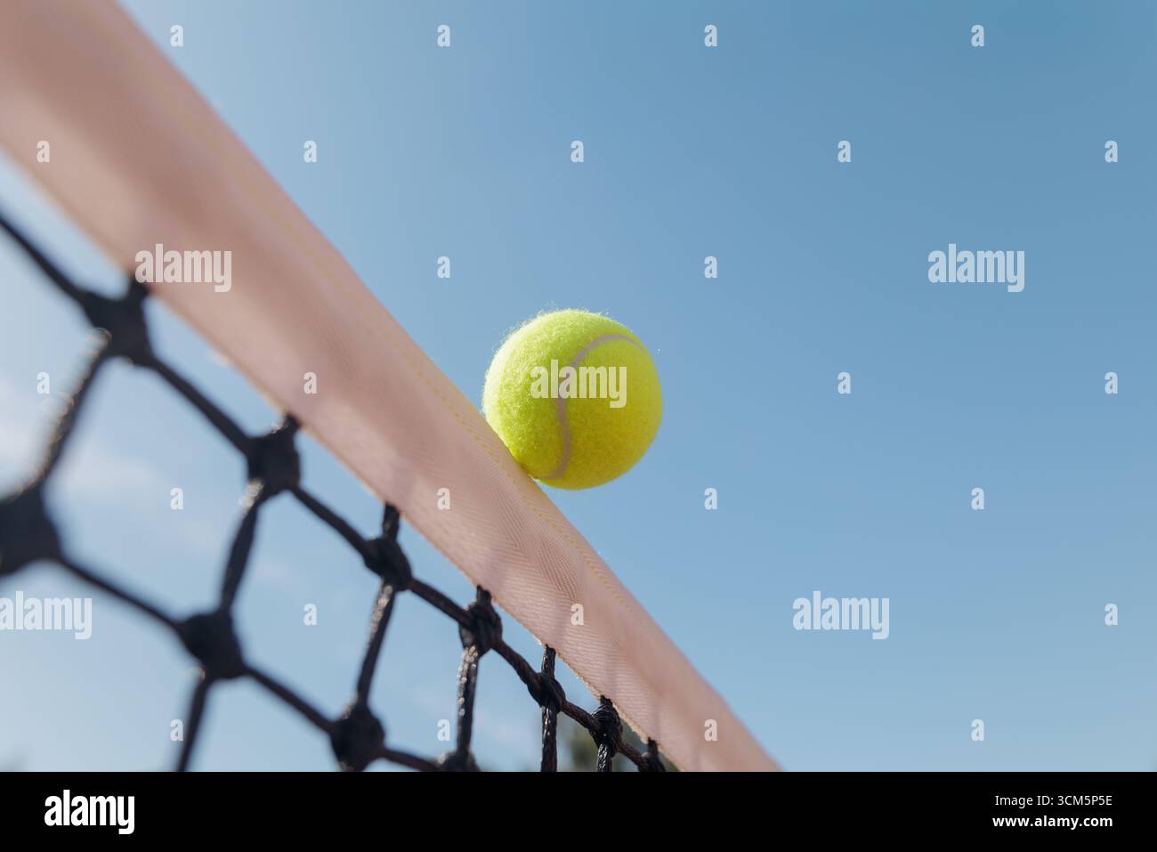 Nahaufnahme eines Tennisballs, der auf der Netzschnur gegen den blauen Himmel ausgeglichen ist, minimales Sportkonzept mit Kopierraum für Banner Stockfoto