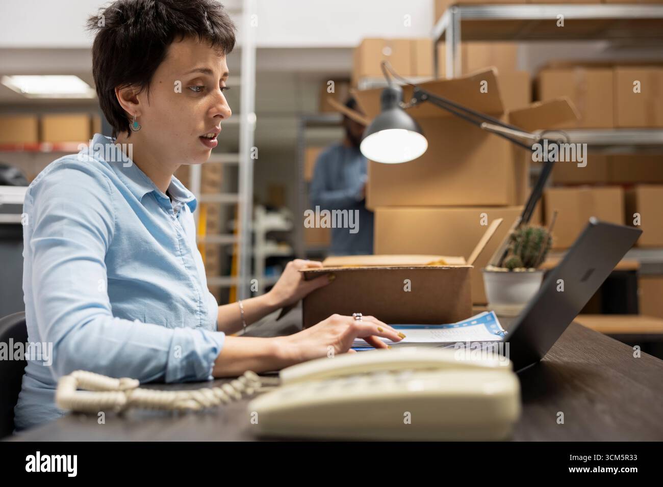 Weibliche Mitarbeiter arbeiten an der effizienten Auftragsabwicklung im E-Commerce-Depot und verwalten Inventar- und Versanddaten, um Pakete für den lokalen und internen Zustelldienst vorzubereiten. Lokale Marke. Stockfoto