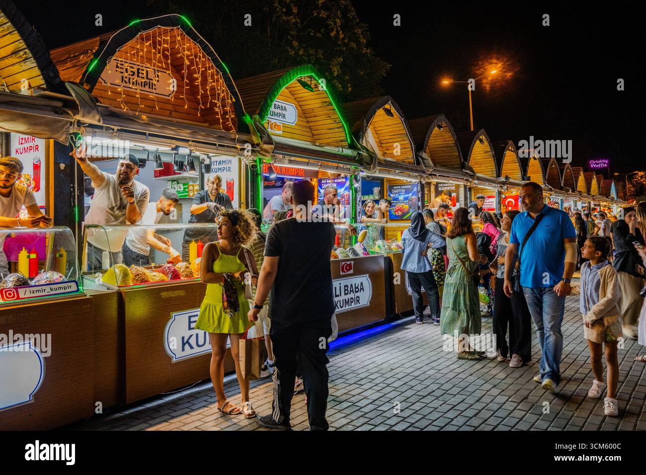 Pulsierende Nachtszene auf einem Kumpir-Lebensmittelmarkt mit bunten Verkaufsständen, lebhaften Händlern und Menschenmassen, die Street Food genießen. Istanbul, Türkiye - 7. August 2023 Stockfoto