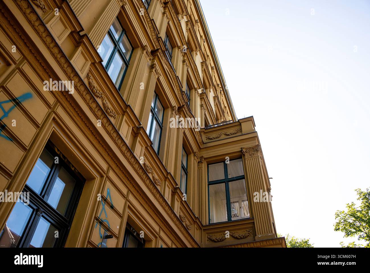 Eine dramatische Tiefwinkelaufnahme eines großen, gelben Altbaugebäudes in Berlin. Die kunstvoll verzierte, historische Fassade erhebt sich vor einem hellen Himmel und fängt das Wesen ein Stockfoto