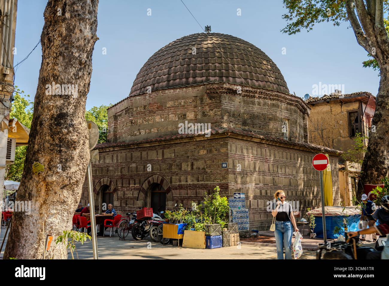 Historisches Backsteinhaus mit Kuppelkuppel in İznik, umgeben von alltäglichem Leben und monumentalen Bäumen, spiegelt den architektonischen und kulturellen Charme der Stadt wider. İzni Stockfoto