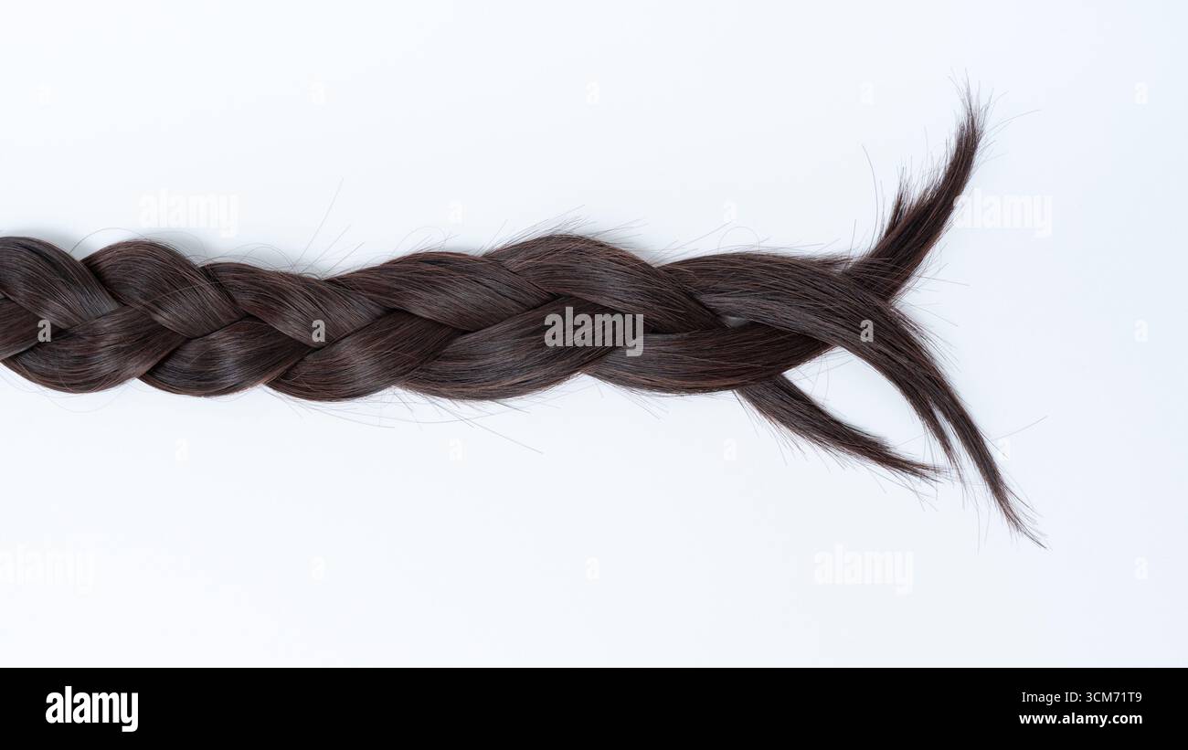 Dunkles geflochtenes Haar, das elegant auf weißem Hintergrund angeordnet ist und die detaillierte Webstruktur und die seidige Textur unterstreicht, ideal für Beauty- und Modethemen Stockfoto