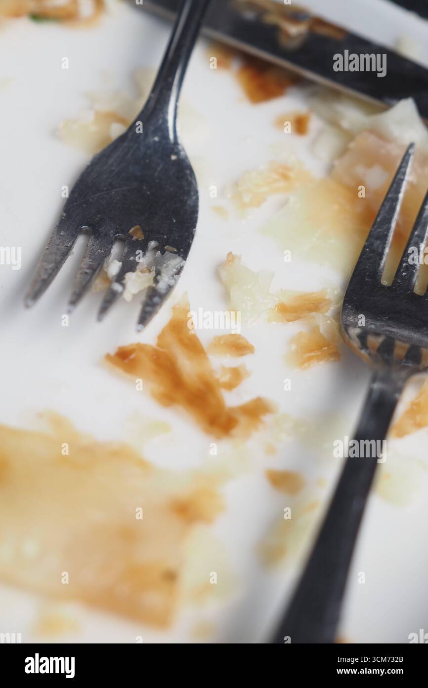 Mehrere Gabeln ruhen auf einem fast leeren Teller nach dem gemeinsamen Abendessen Stockfoto
