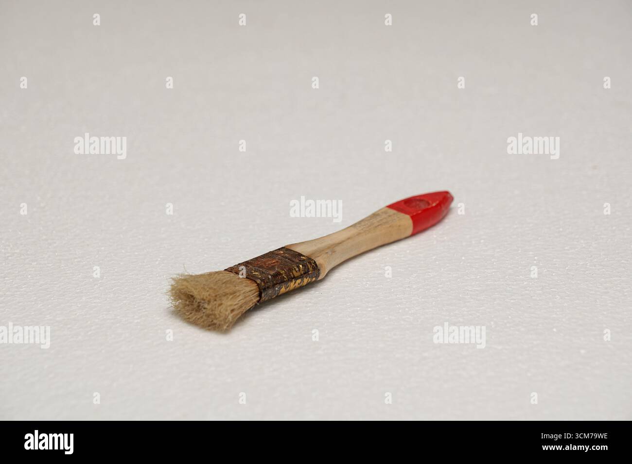 Ein kleiner Pinsel mit Holzgriff und roter Spitze mit weichen Borsten, die auf einer weißen Oberfläche aufliegen Stockfoto