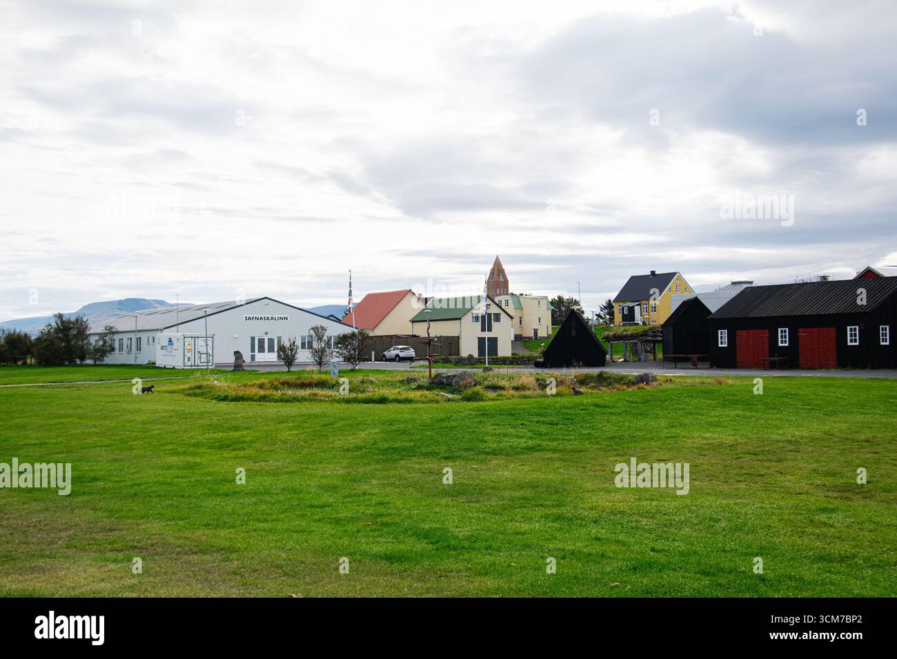 Akranes, Island - 12. September 2025: Grüne Felder und traditionelle Gebäude in Akranes, Island, unter einem bewölkten Himmel, Safnaskálinn Volksmuseum. Stockfoto