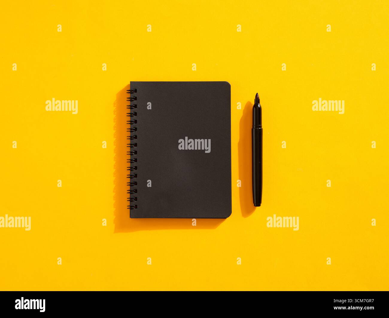 Schwarzes, spiralgebundenes Notizbuch und Stift auf gelbem Hintergrund, repräsentieren Kreativität, Notizen und Planung Stockfoto