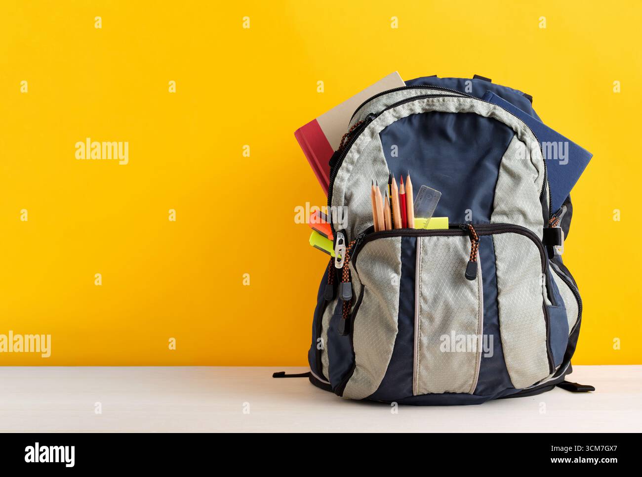 Rucksack voller Schulutensilien wie Notizbücher, Bleistifte, Lineal und Textmarker auf gelbem Hintergrund mit Kopierraum. Back-to-School-Konzept. Stockfoto