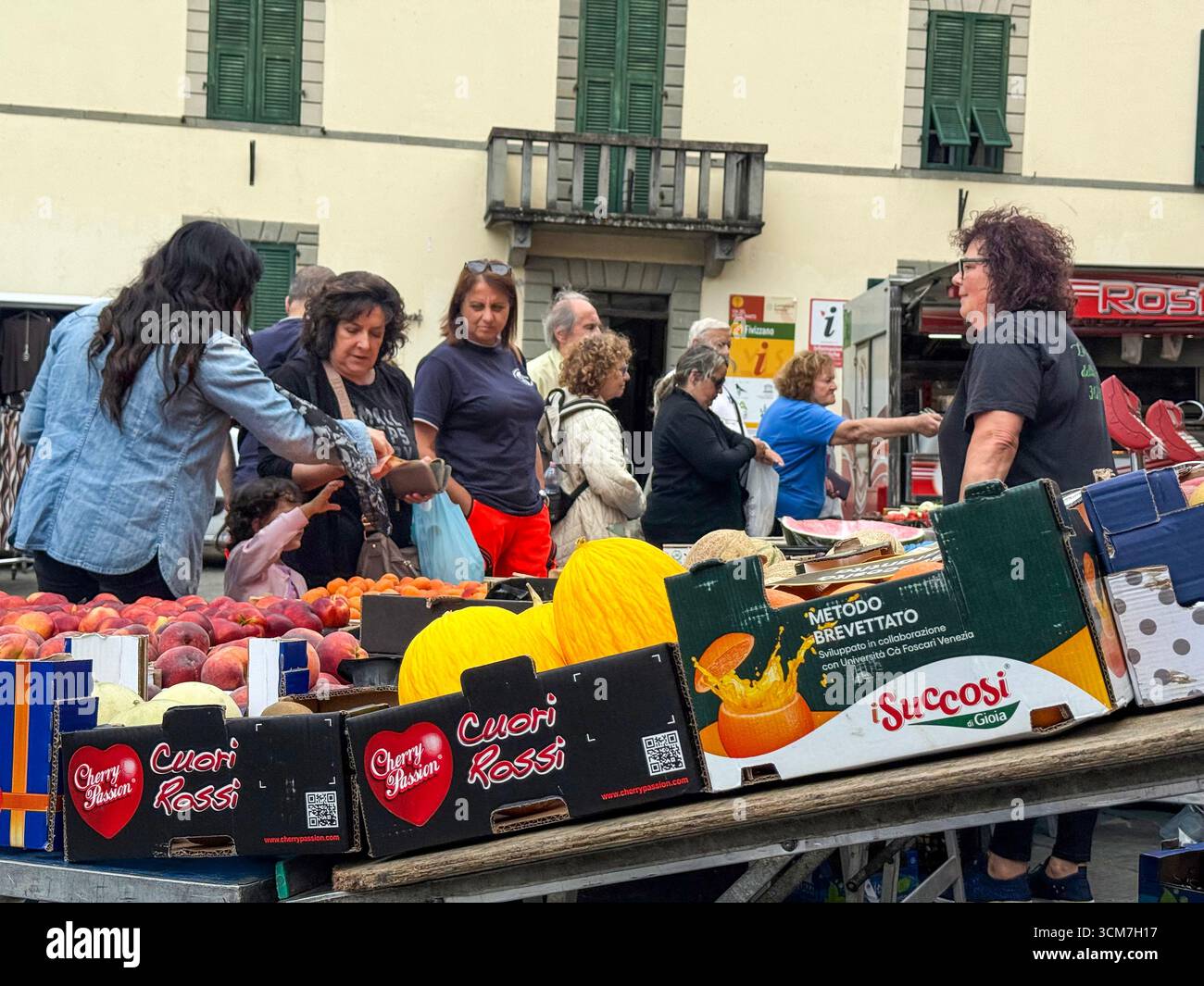 Ein geschäftiger Obst- und Gemüsestand auf dem Wochenmarkt vor der Chiesa del S. Jacopo e Antonio (Kirche S. und Antonio auf der Piazza aus dem 16. Jahrhundert) - Smartphone-aufgenommenes Stockfoto