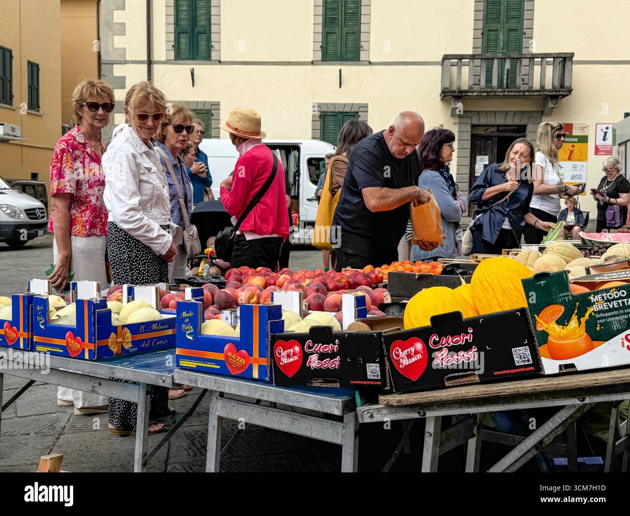 Ein geschäftiger Obst- und Gemüsestand auf dem Wochenmarkt vor der Chiesa del S. Jacopo e Antonio (Kirche S. und Antonio auf der Piazza aus dem 16. Jahrhundert) - Smartphone-aufgenommenes Stockfoto