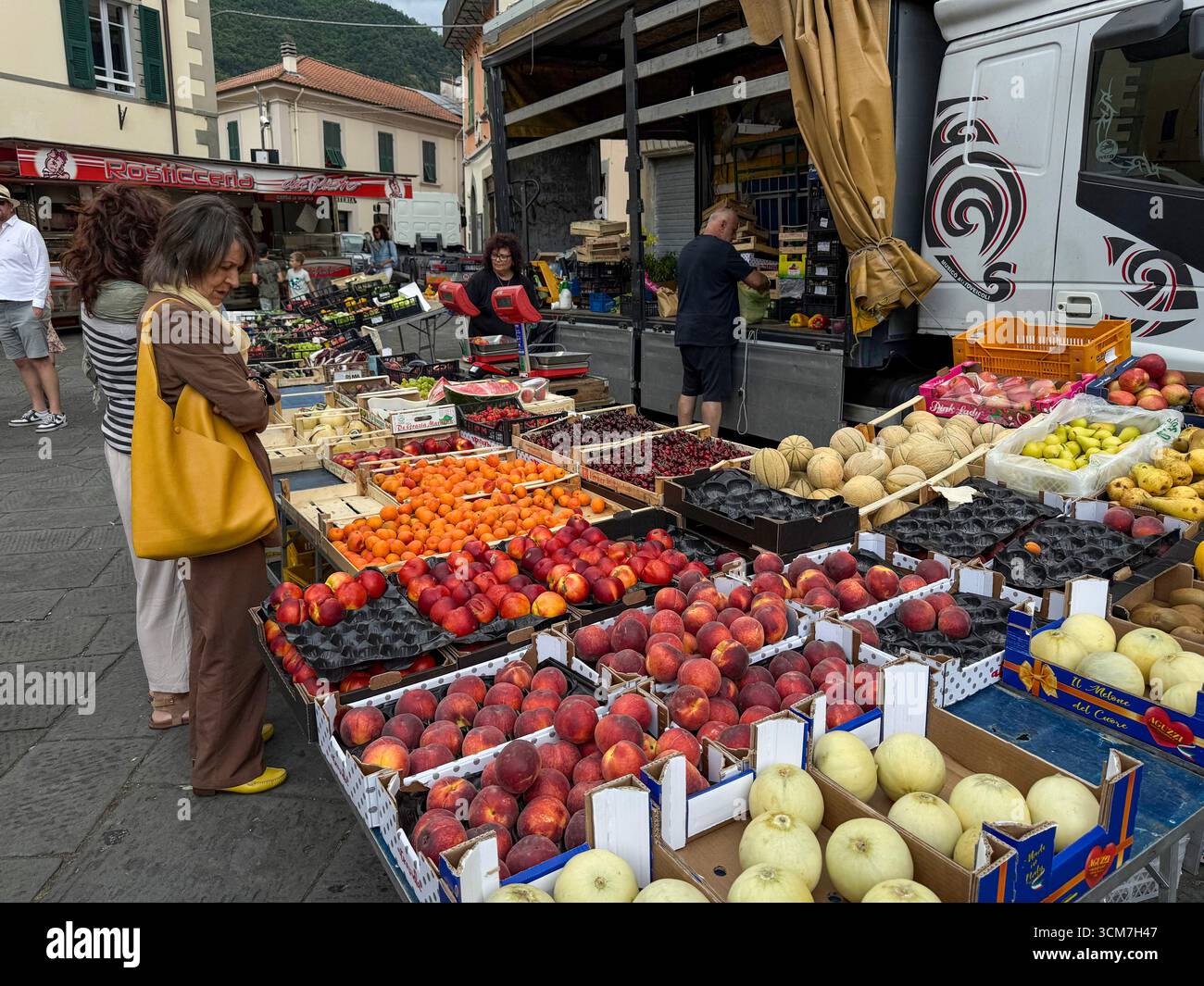Ein geschäftiger Obst- und Gemüsestand auf dem Wochenmarkt vor der Chiesa del S. Jacopo e Antonio (Kirche S. und Antonio auf der Piazza aus dem 16. Jahrhundert) - Smartphone-aufgenommenes Stockfoto