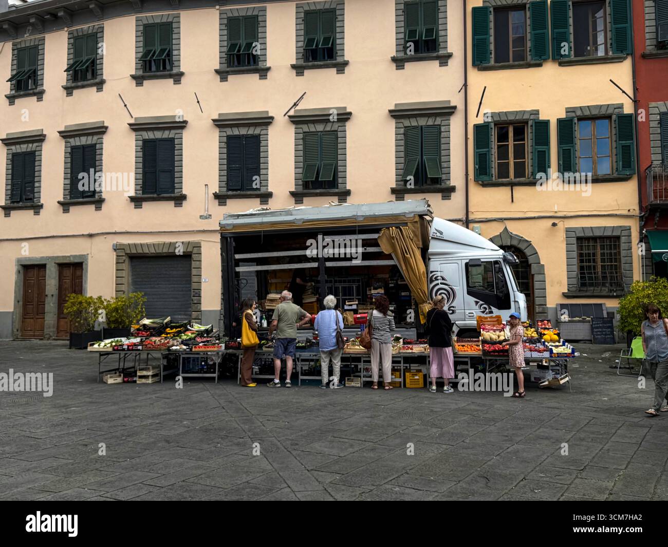 Ein geschäftiger Obst- und Gemüsestand auf dem Wochenmarkt auf der Piazza Medice aus dem 16. Jahrhundert in der mittelalterlichen Stadt Fivizzano, einer Gemeinde in der Provinz M. - Smartphone-aufgenommenes Stockfoto