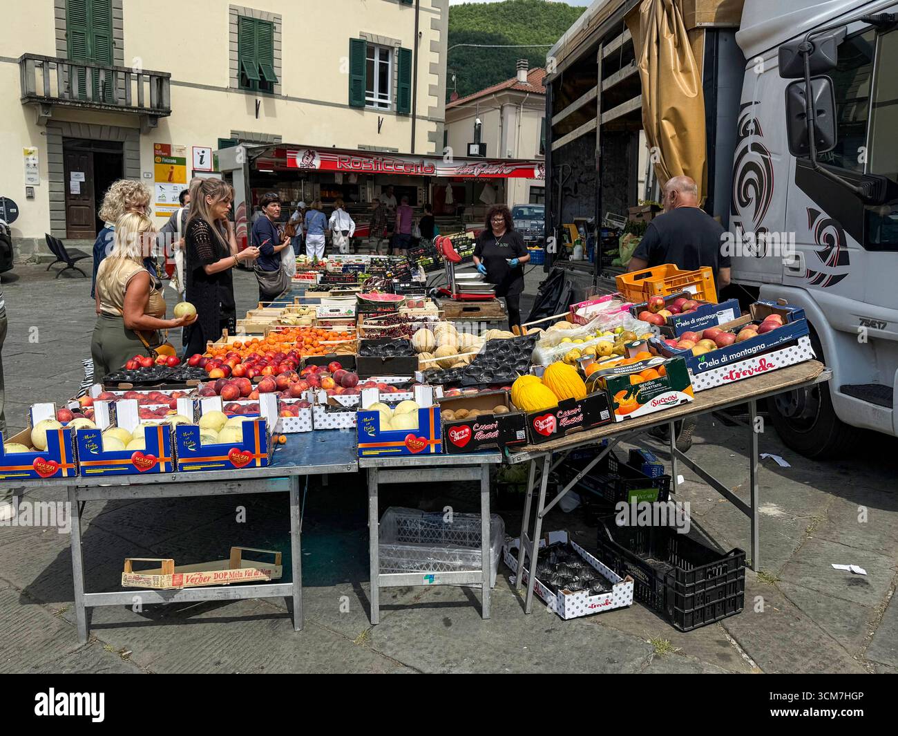 Ein geschäftiger Obst- und Gemüsestand auf dem Wochenmarkt auf der Piazza Medice aus dem 16. Jahrhundert in der mittelalterlichen Stadt Fivizzano, einer Gemeinde in der Provinz M. - Smartphone-aufgenommenes Stockfoto