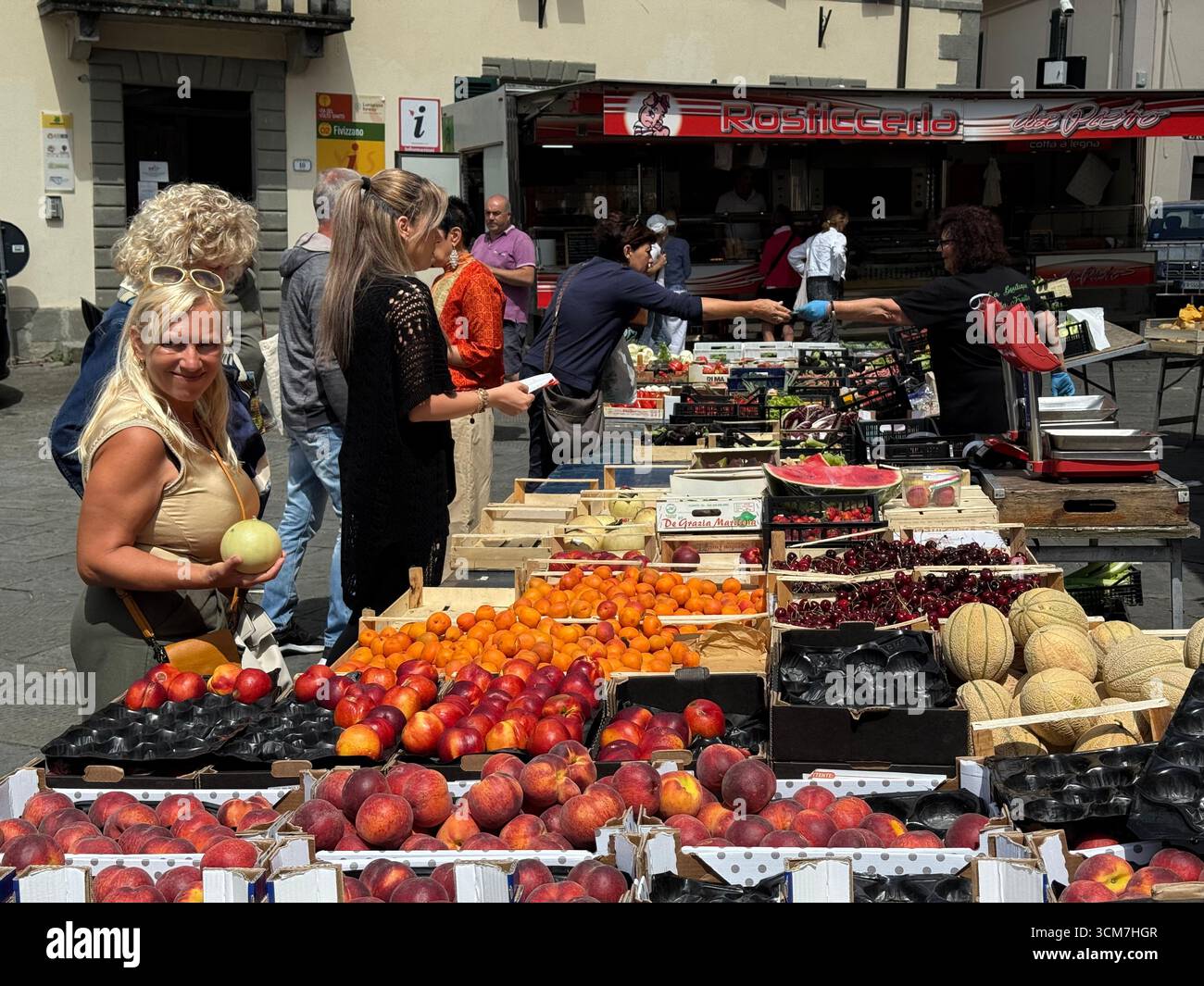 Ein geschäftiger Obst- und Gemüsestand auf dem Wochenmarkt auf der Piazza Medice aus dem 16. Jahrhundert in der mittelalterlichen Stadt Fivizzano, einer Gemeinde in der Provinz M. - Smartphone-aufgenommenes Stockfoto