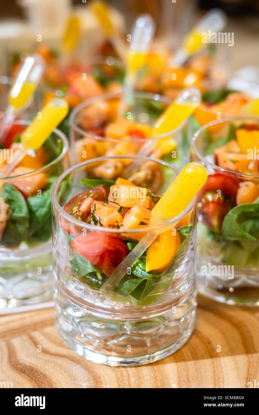 Frischer Salat mit Tomaten, Pfirsich und Gemüse im Glas mit einer Pipette mit gelber Soße. Stockfoto
