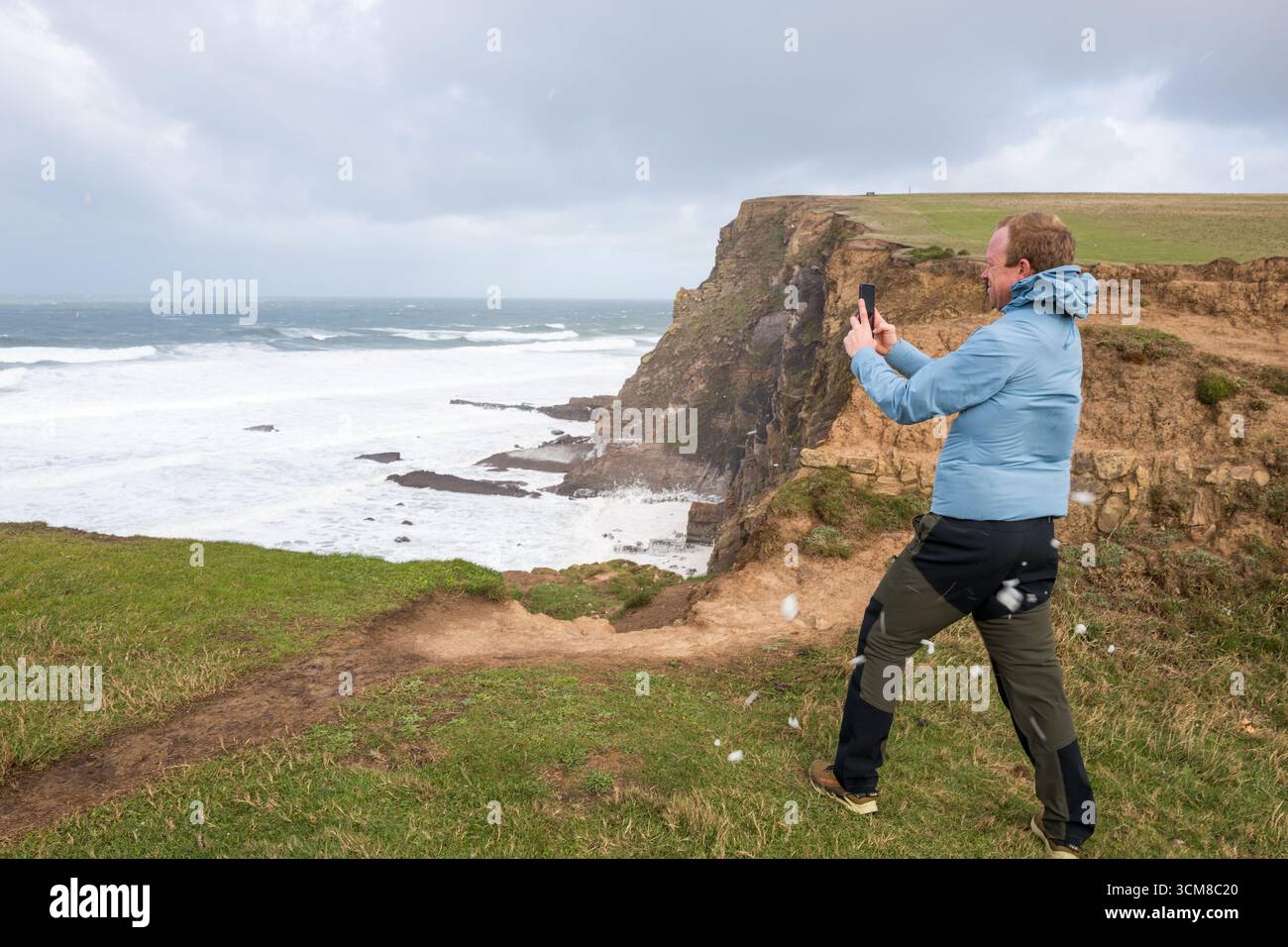 UK. Wetter, Bude, Cornwall, Großbritannien. September 2025. Ein Mann, der es schwer hat, sich gerade gegen die sehr starken Winde und den Meeresschaum zu stellen, während er ein Foto macht. Quelle: Alan Beastall/Alamy Live News Stockfoto
