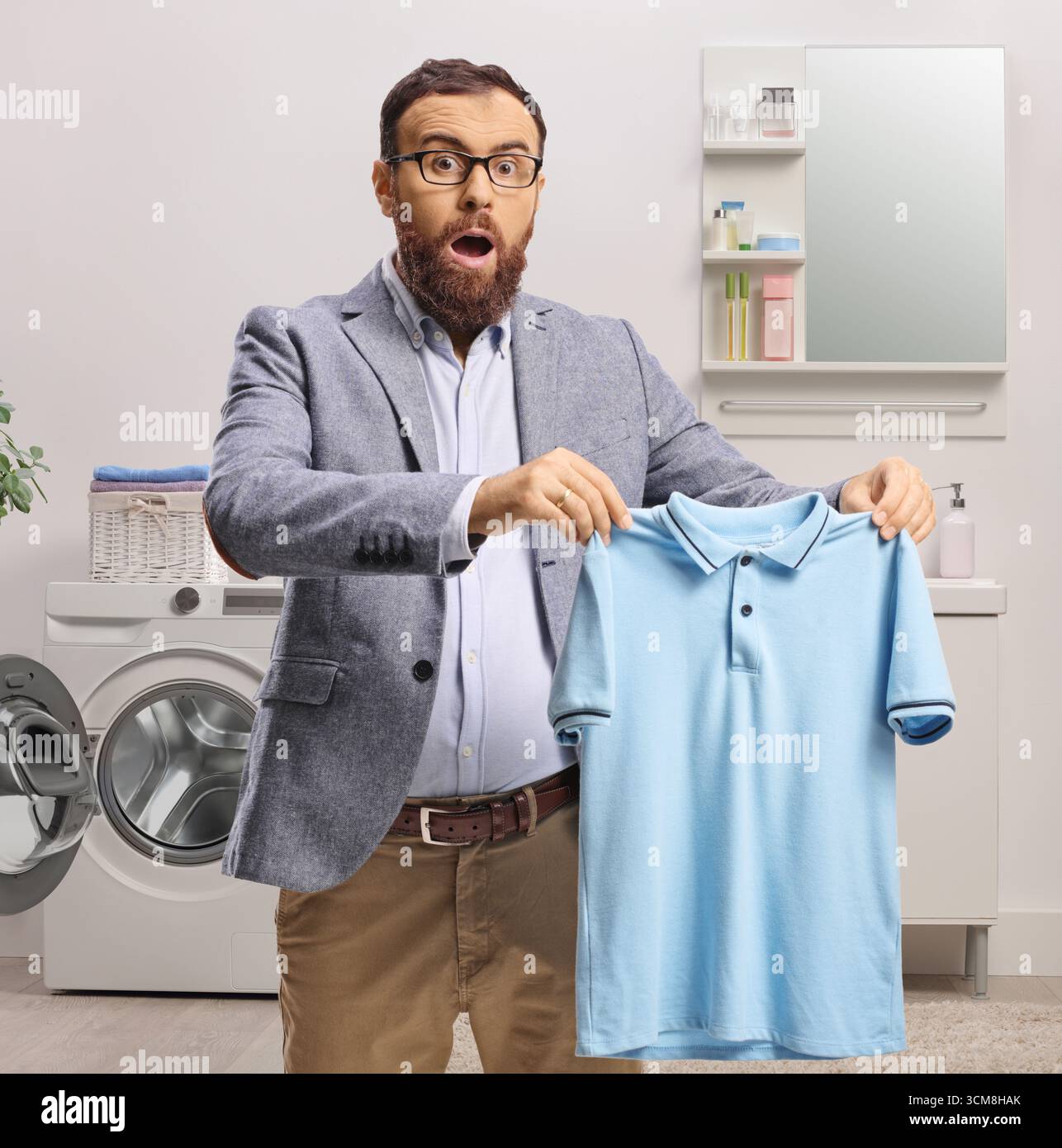 Überraschter Mann, der ein blaues T-Shirt im Badezimmer hält Stockfoto