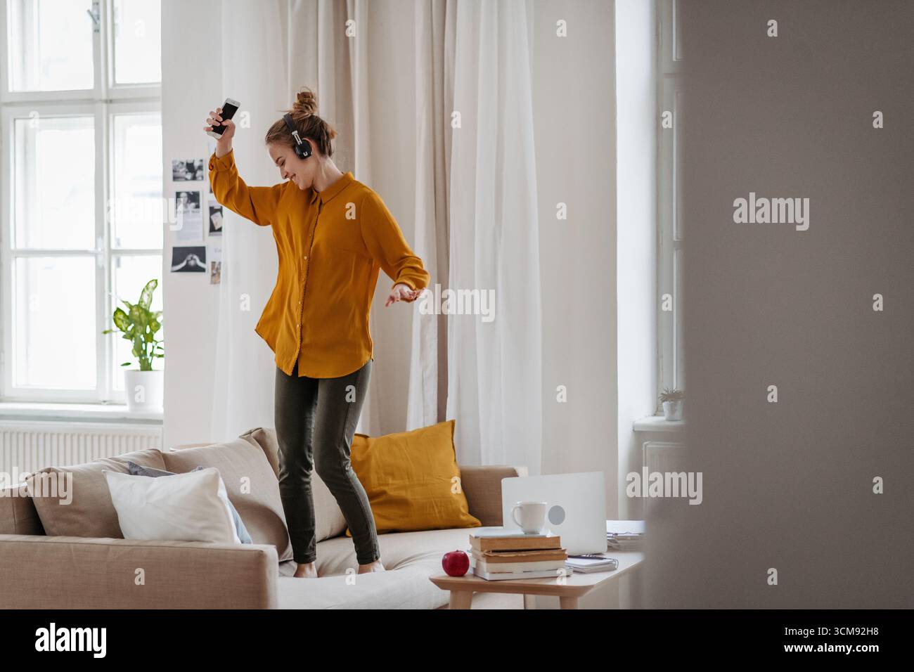 Junge Frau tanzt auf Sofa mit Kopfhörern. Stockfoto