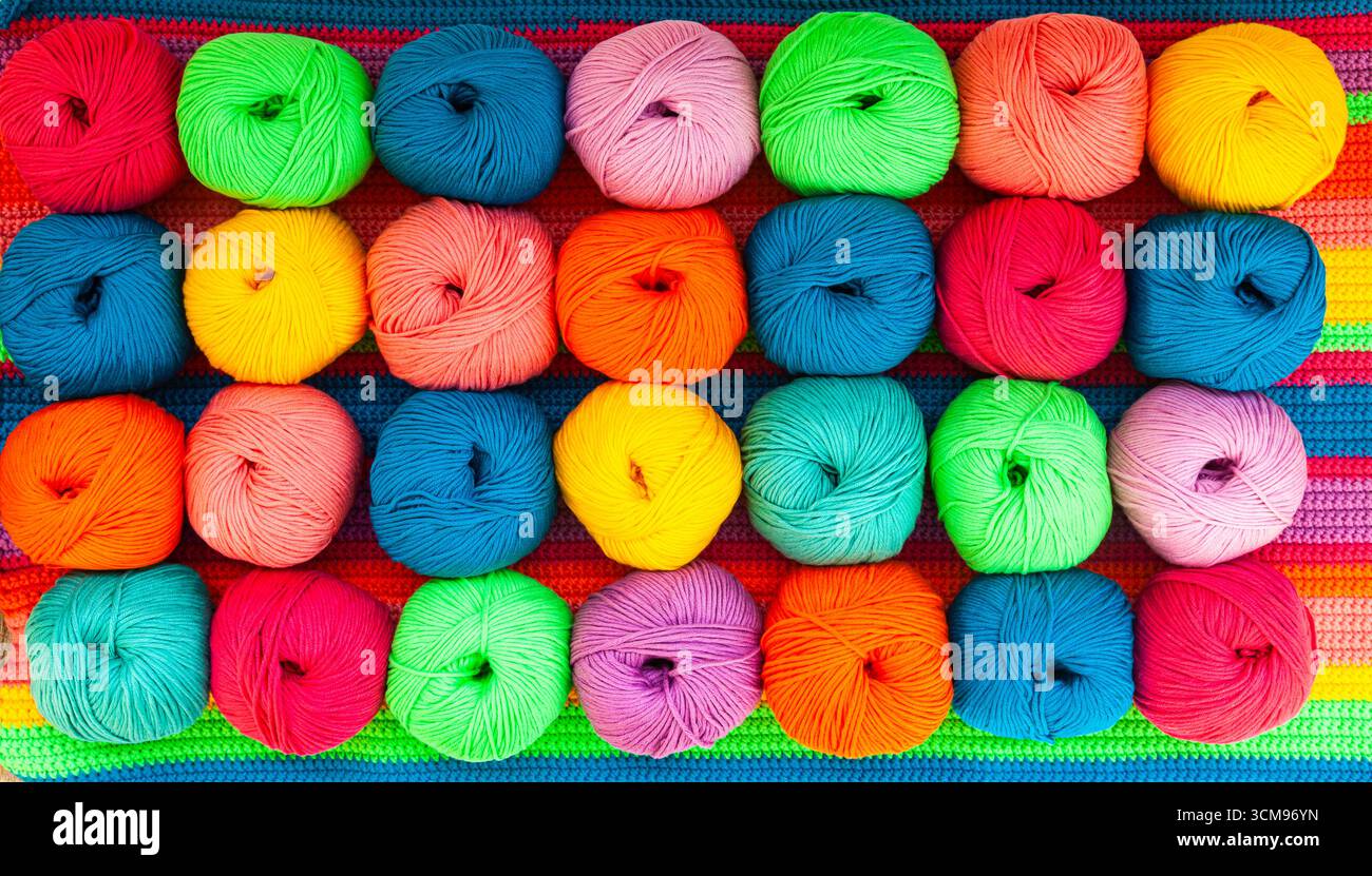 Viele bunte Garnknäuel auf einem gestrickten Stoff, Nahaufnahme. Stockfoto