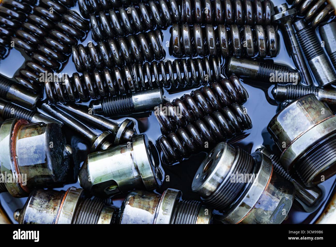 Mechanische Stahlteile mit Maschinenöl geschmiert, Nahaufnahme. Stahleinspritzdüsen, Federn, Buchsen, Bolzen und Gewindeteile in Öl. Stockfoto