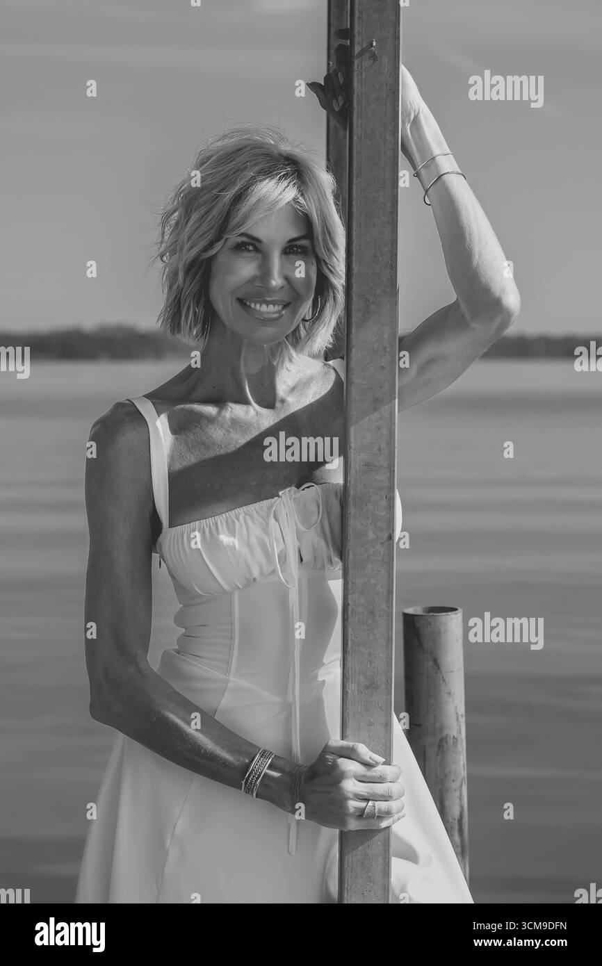 Eine schöne blonde Frau steht selbstbewusst, ihr strahlendes Lächeln und ihr ausgeglichenes Auftreten strahlen Eleganz aus. Ihre anmutige Haltung unterstreicht ihren Charme, Kreatin Stockfoto