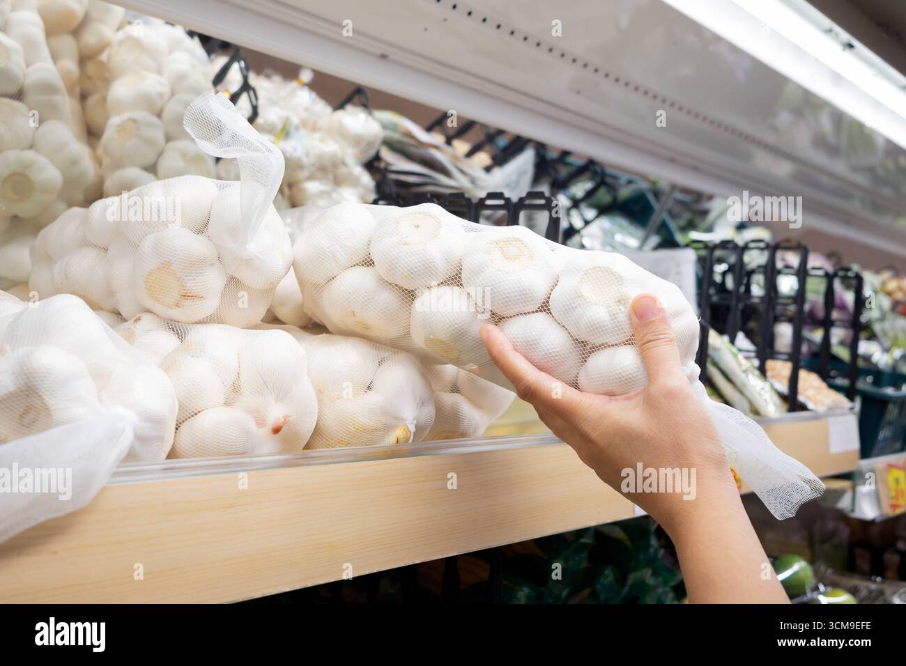 Die Hand eines Käufers holt einen Haufen Knoblauch aus dem Lebensmittelgeschäft. Stockfoto