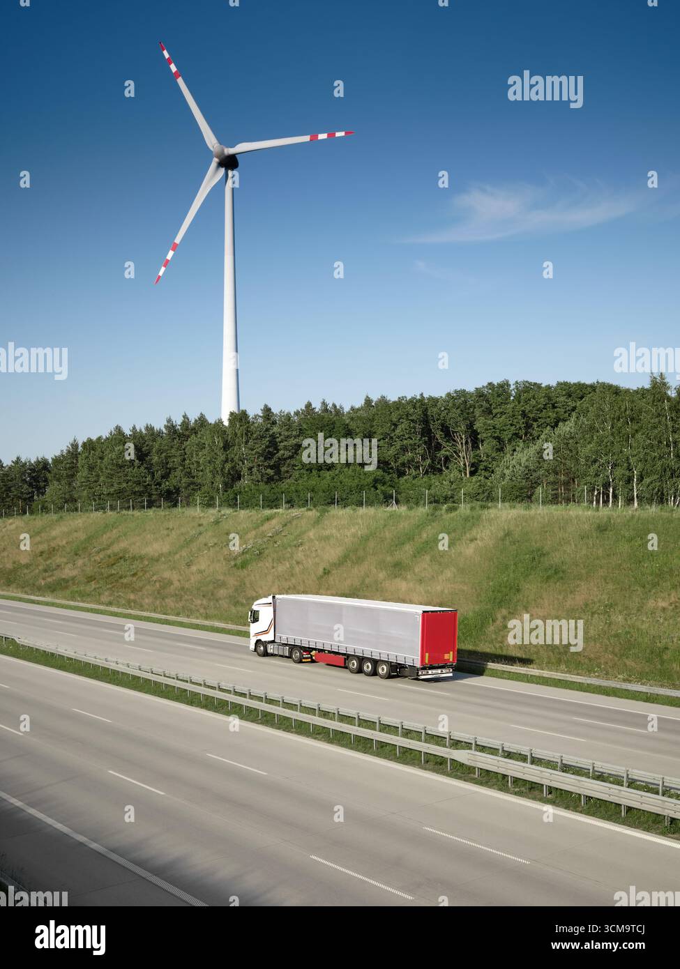 Lkw fahren auf der Autobahn mit Windkraftanlage im Hintergrund, Konzept erneuerbarer Energien und grüner Logistik. Stockfoto