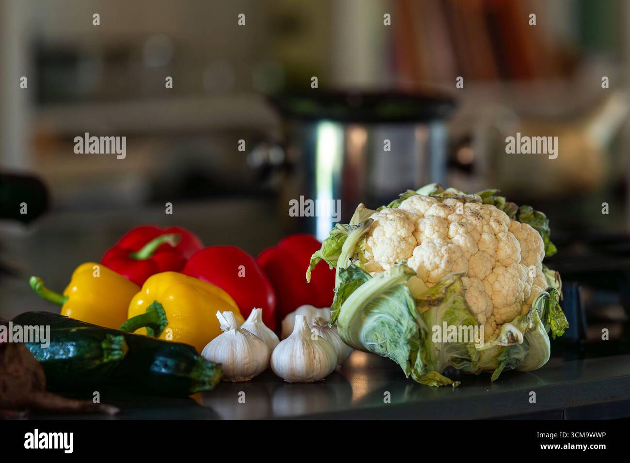 Auswahl an frischem Gemüse auf einem Küchentisch. Farbenfrohe Gemüsepräsentation mit Zucchini, Paprika, Knoblauch und Blumenkohl. Stockfoto