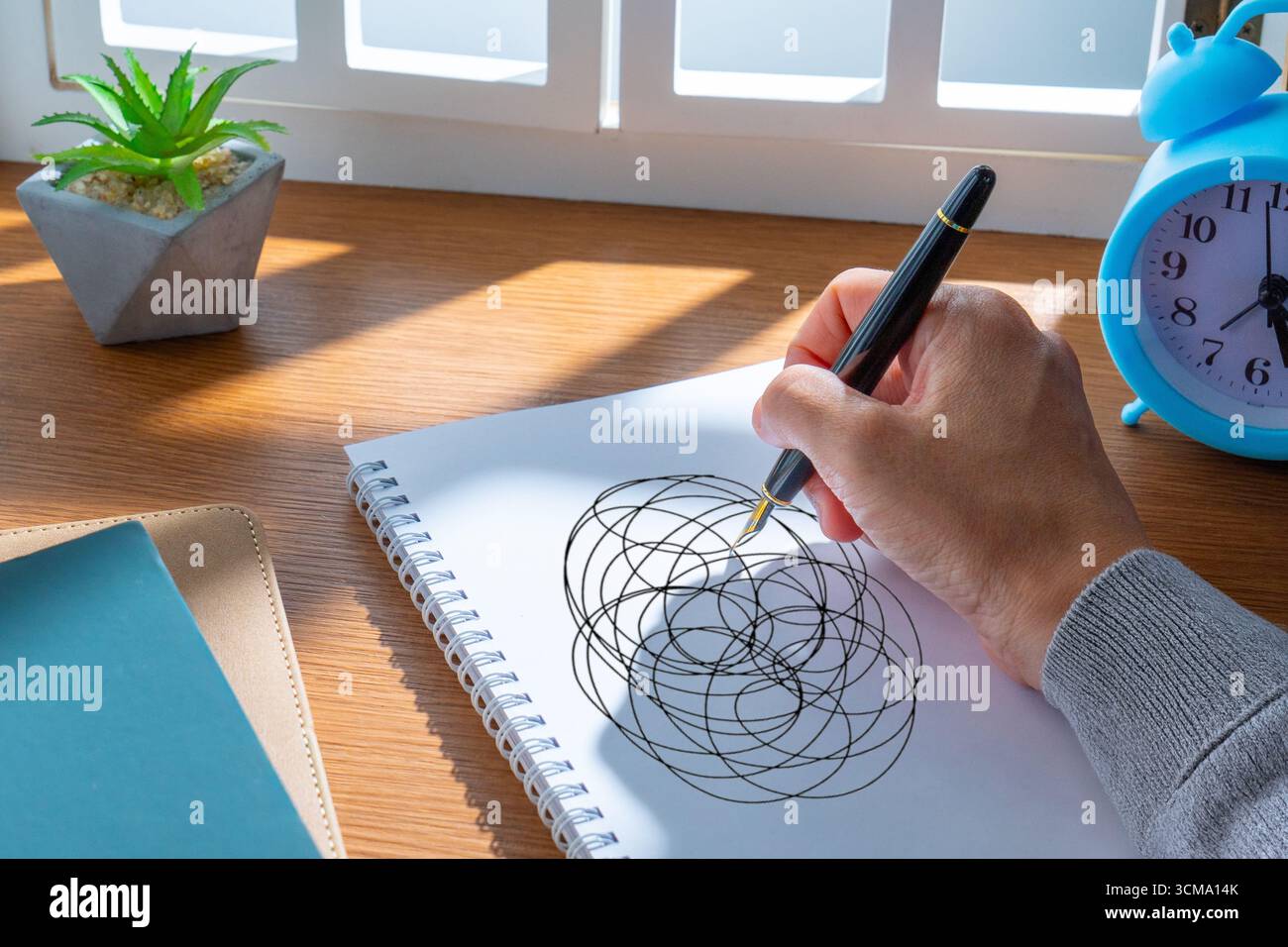 Eine Hand, die einen Stift benutzt, um chaotische, verworrene Kreise auf einen leeren Notizblock zu kritzeln. Stress, mentales Chaos und überdenkendes Konzept. Stockfoto