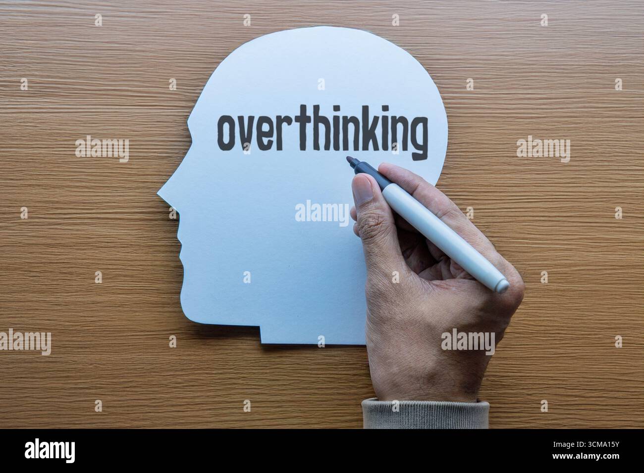 Eine Hand schreibt das Wort "überdenken" auf einen Papierausschnitt, der wie ein menschlicher Kopf geformt ist. Psychische Gesundheit, Psychologie und persönliches Wohlbefinden. Stockfoto