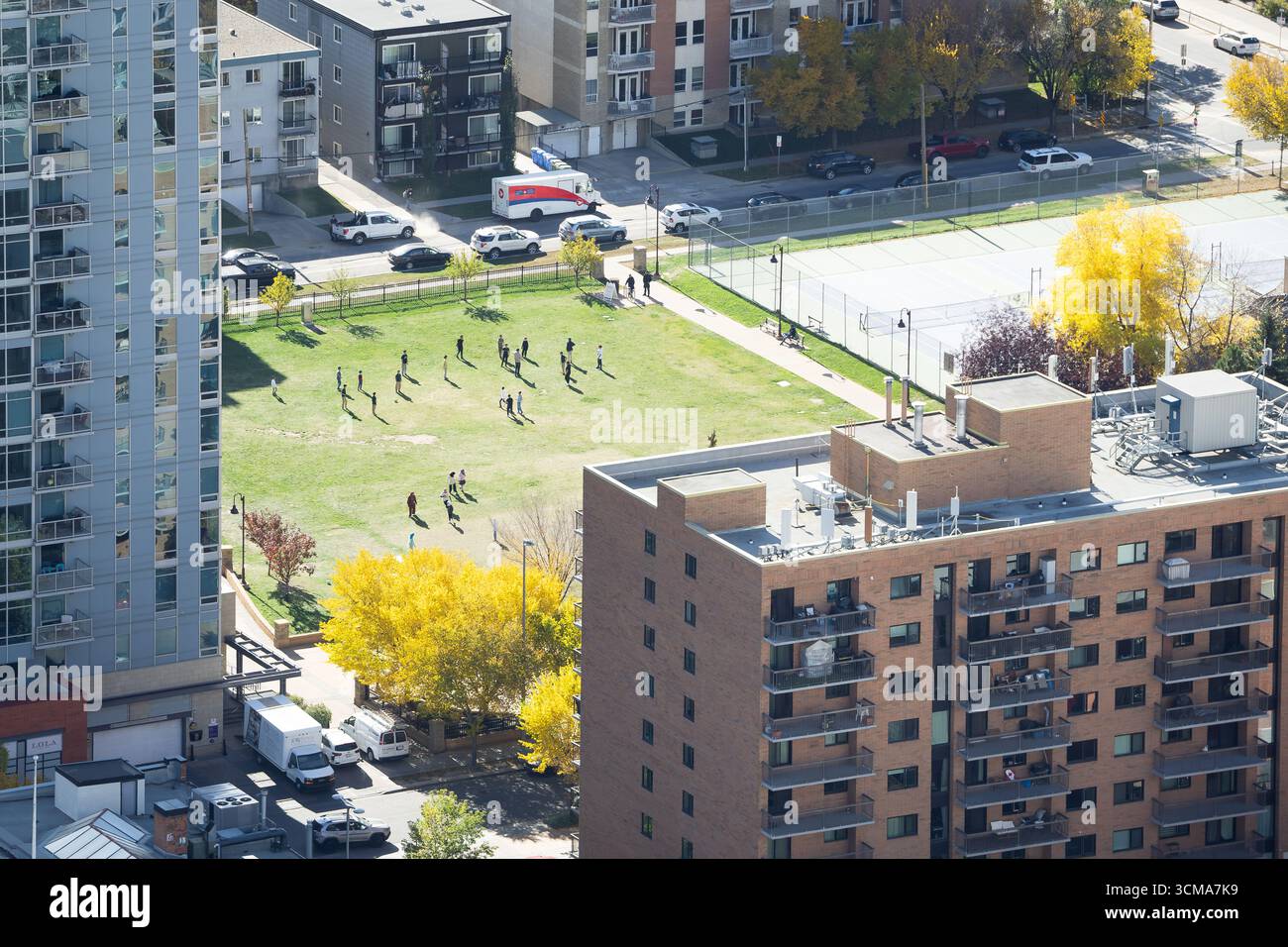 Entfernter Schulhof in der Innenstadt, auf dem Kinder auf dem Fußballplatz spielen und die Apartmentgebäude mit Bäumen in Herbstfarben überblicken. Stockfoto