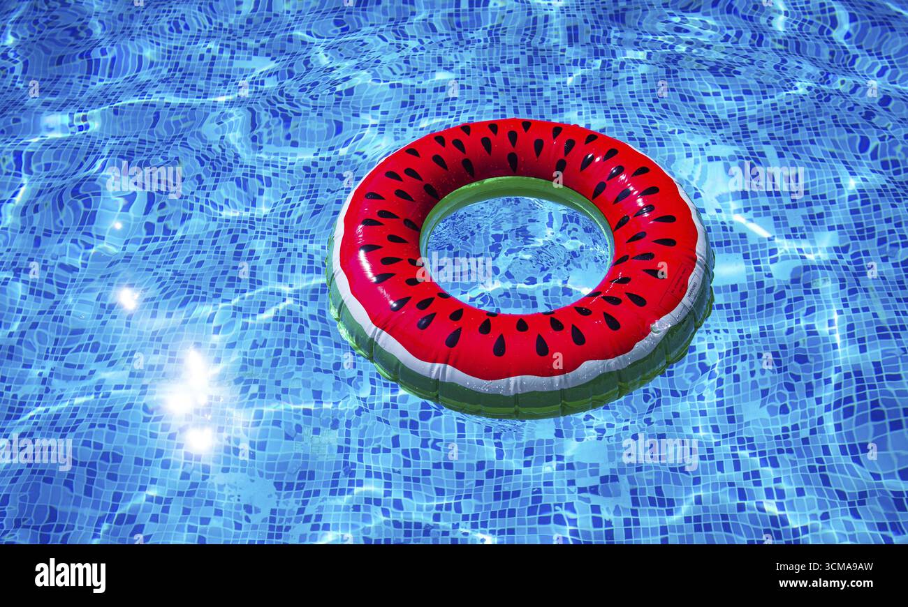 Ein heller Ring - ein Schwimmer, mit einer Wassermelone, im klaren blauen Wasser des Pools, unter dem Sonnenlicht Stockfoto