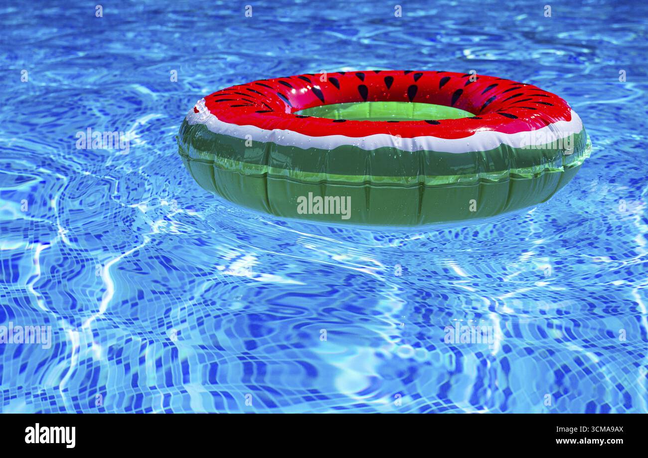 Ein heller Ring - ein Schwimmer, mit einer Wassermelone, im klaren blauen Wasser des Pools, unter dem Sonnenlicht Stockfoto