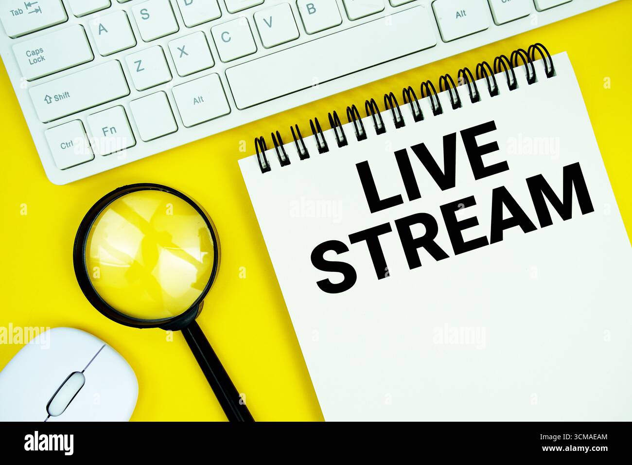 Notizblock mit dem Text „Live Stream“ und weißer Tastatur, kabelloser Maus, Lupe auf gelbem Hintergrund Stockfoto