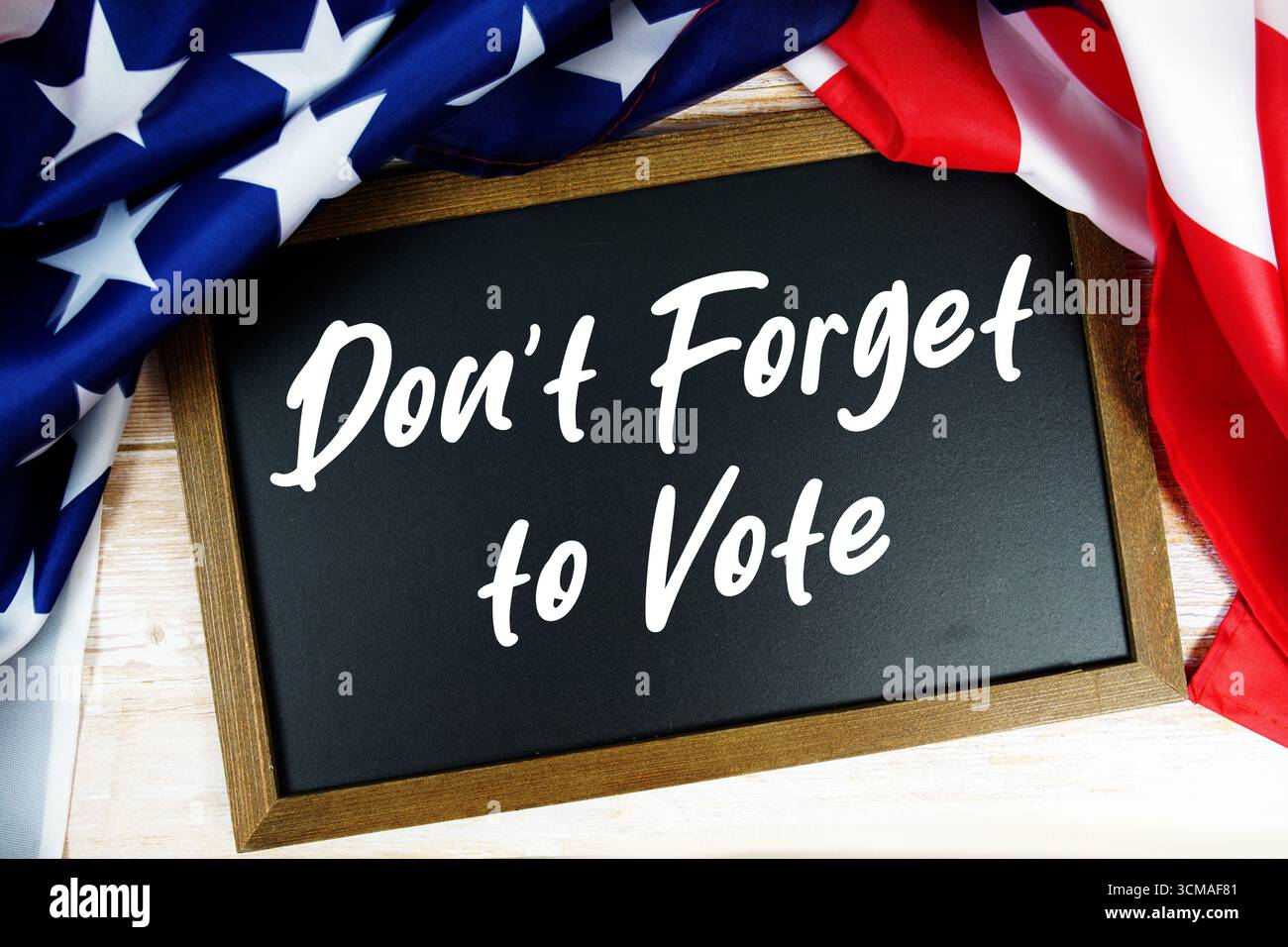 Amerikanische Flagge mit Tafel „Vergessen Sie nicht, zu wählen“ auf hölzernem Hintergrund Stockfoto