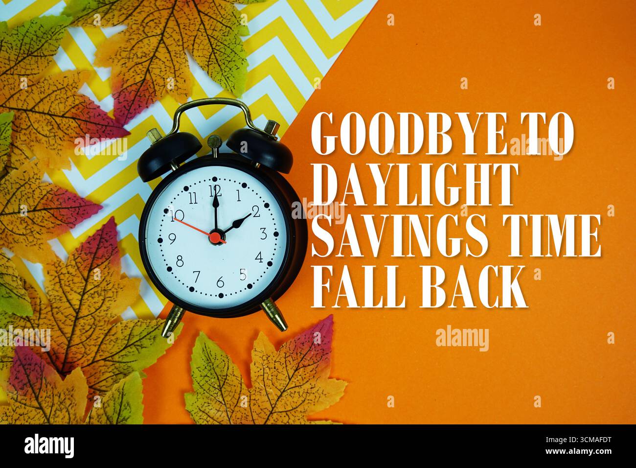 Verabschieden Sie sich von der Sommerzeit mit Wecker und Ahornblättern auf orangem Hintergrund Stockfoto